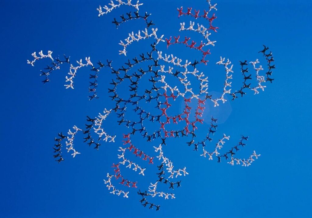 Large group of skydivers flying in formation of flower against blue sky